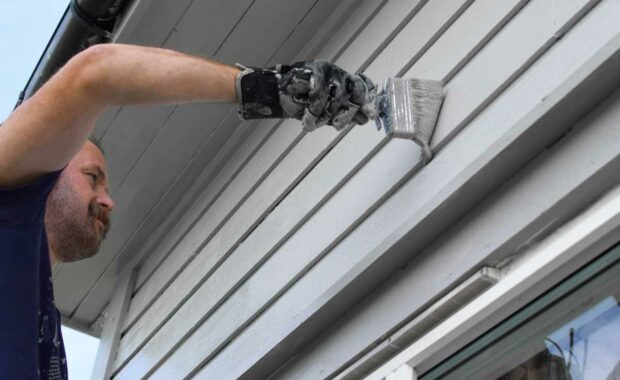Painter painting the exterior of a gray home